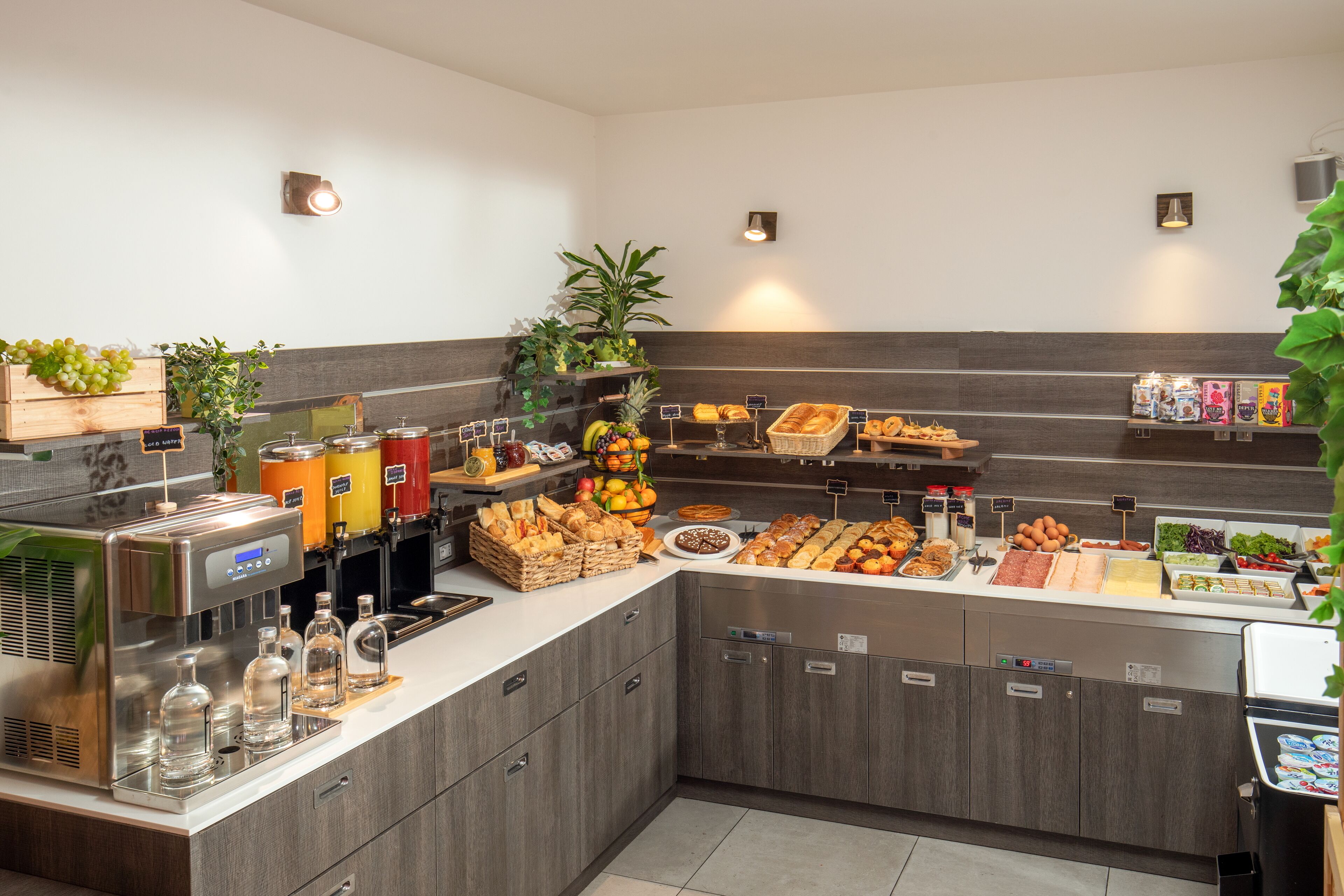 A buffet area with various food items, a beverage dispenser, and a refrigerator.