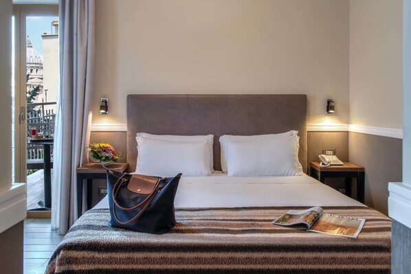 A hotel room with a bed, a nightstand, a lamp, a handbag, and a magazine on the bed.