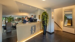 A reception desk with a modern design, a large potted plant, and a mirror with an ornate frame. - Fragrance Hotel St. Peter (Rome)
