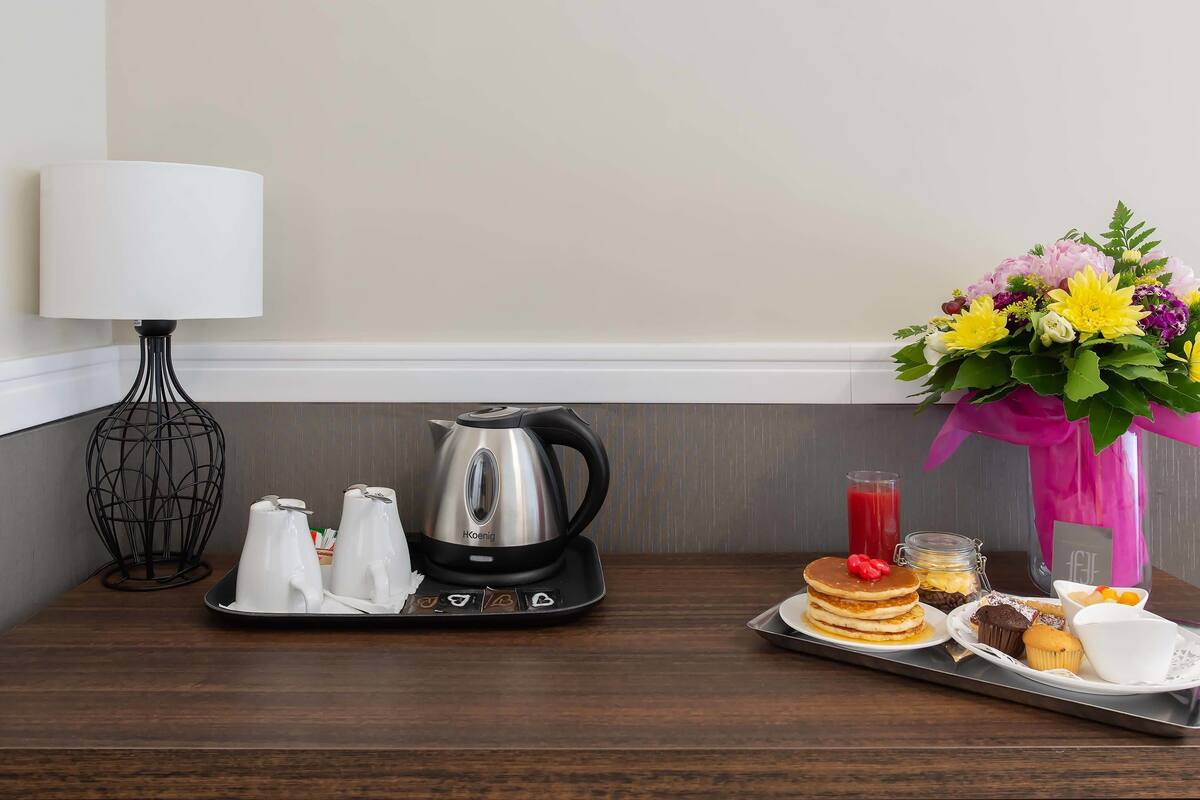 A breakfast tray with pancakes, muffins, and a coffee pot on a wooden table.