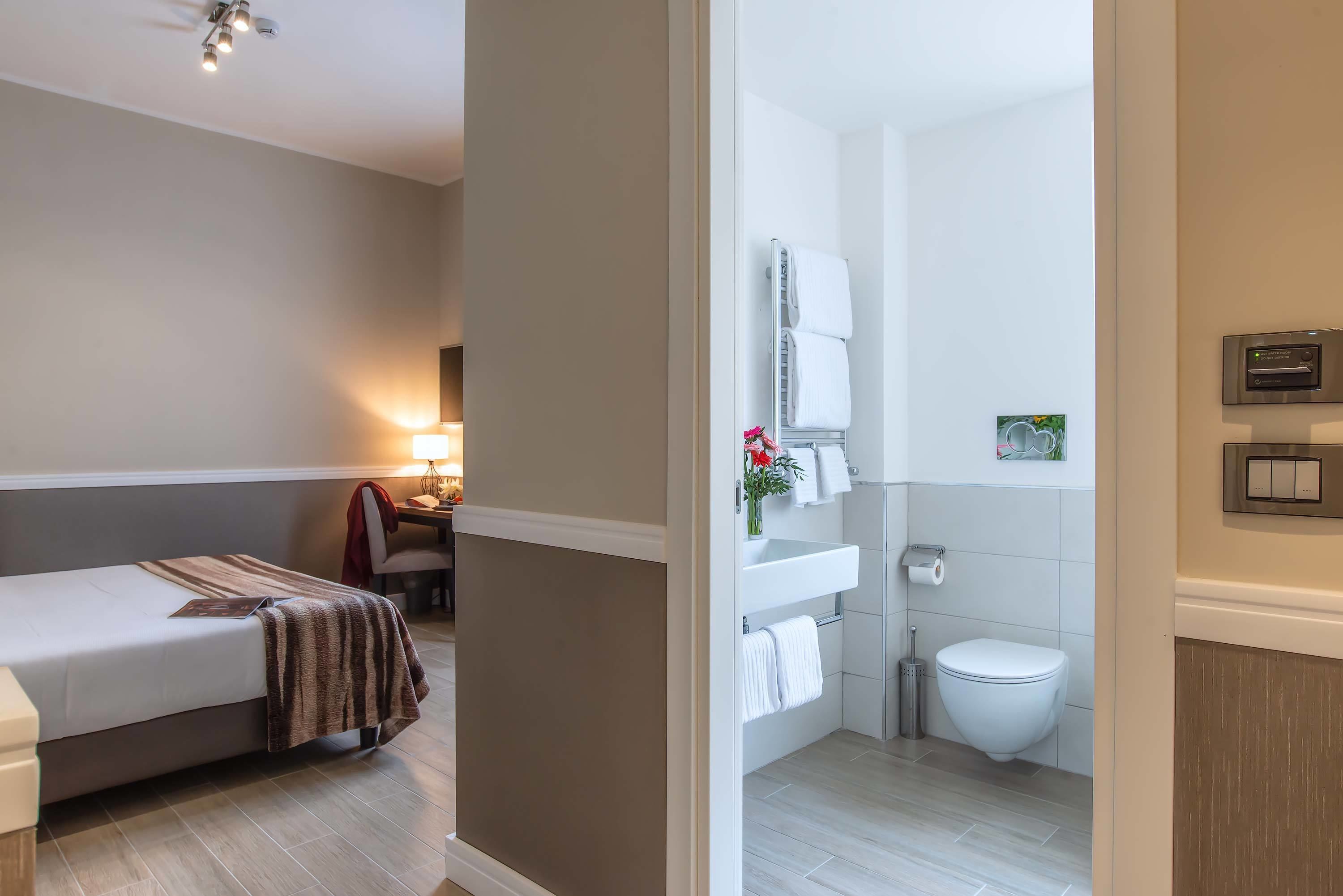 A hotel room with a bed, bedside table, lamp, and a view into the bathroom.