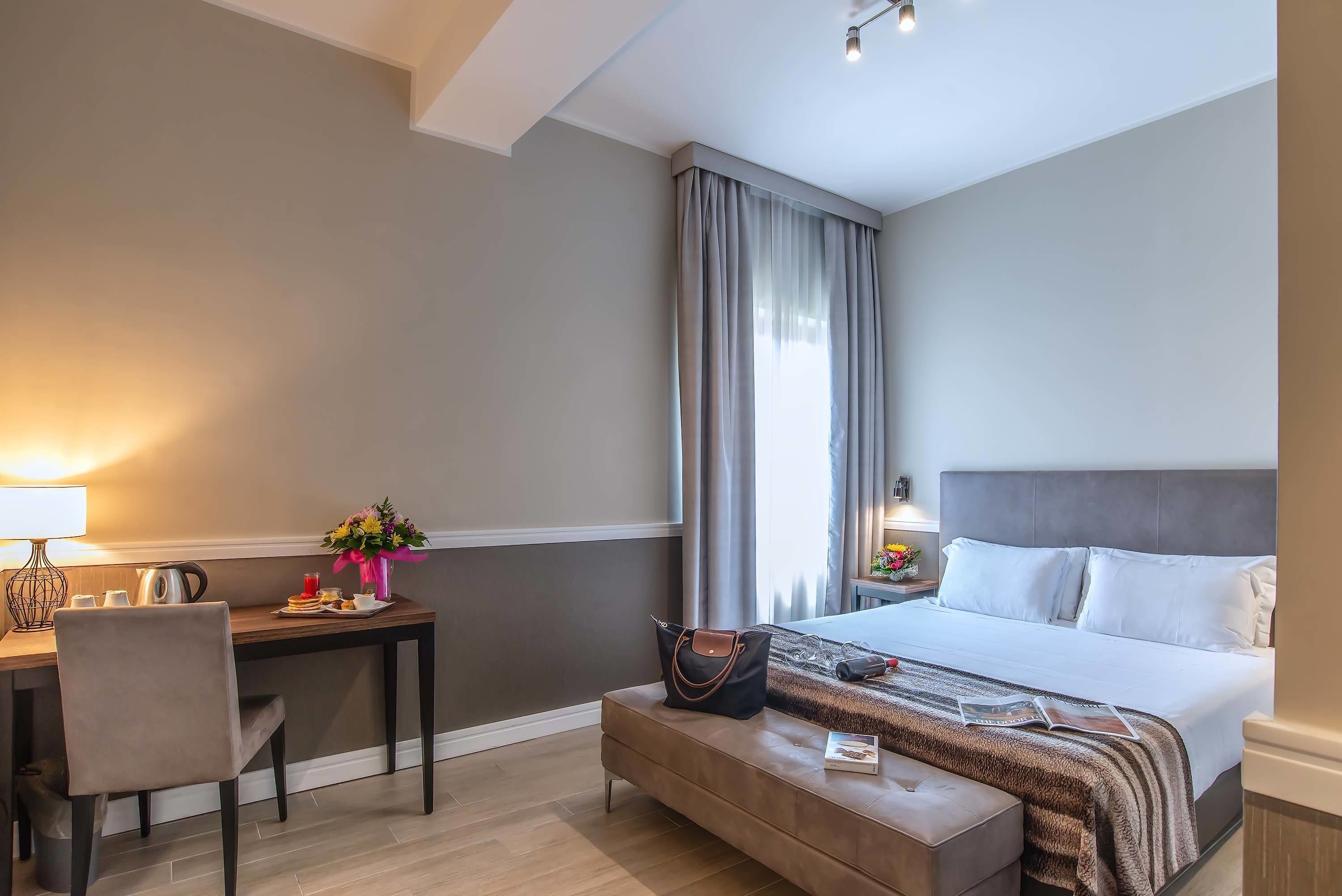 Une chambre d’hôtel comprenant un lit, une table de chevet, un bureau, une chaise et une petite table avec une lampe et des fleurs.