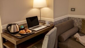 A hotel room with a wooden desk, a laptop, a kettle, a cup, and a plate with food. - Fragrance Hotel St. Peter (Rome)