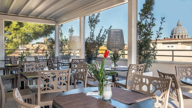 An outdoor seating area with tables and chairs, a view of a cityscape including a dome structure, and decorative plants. - Fragrance Hotel St. Peter (Rome)