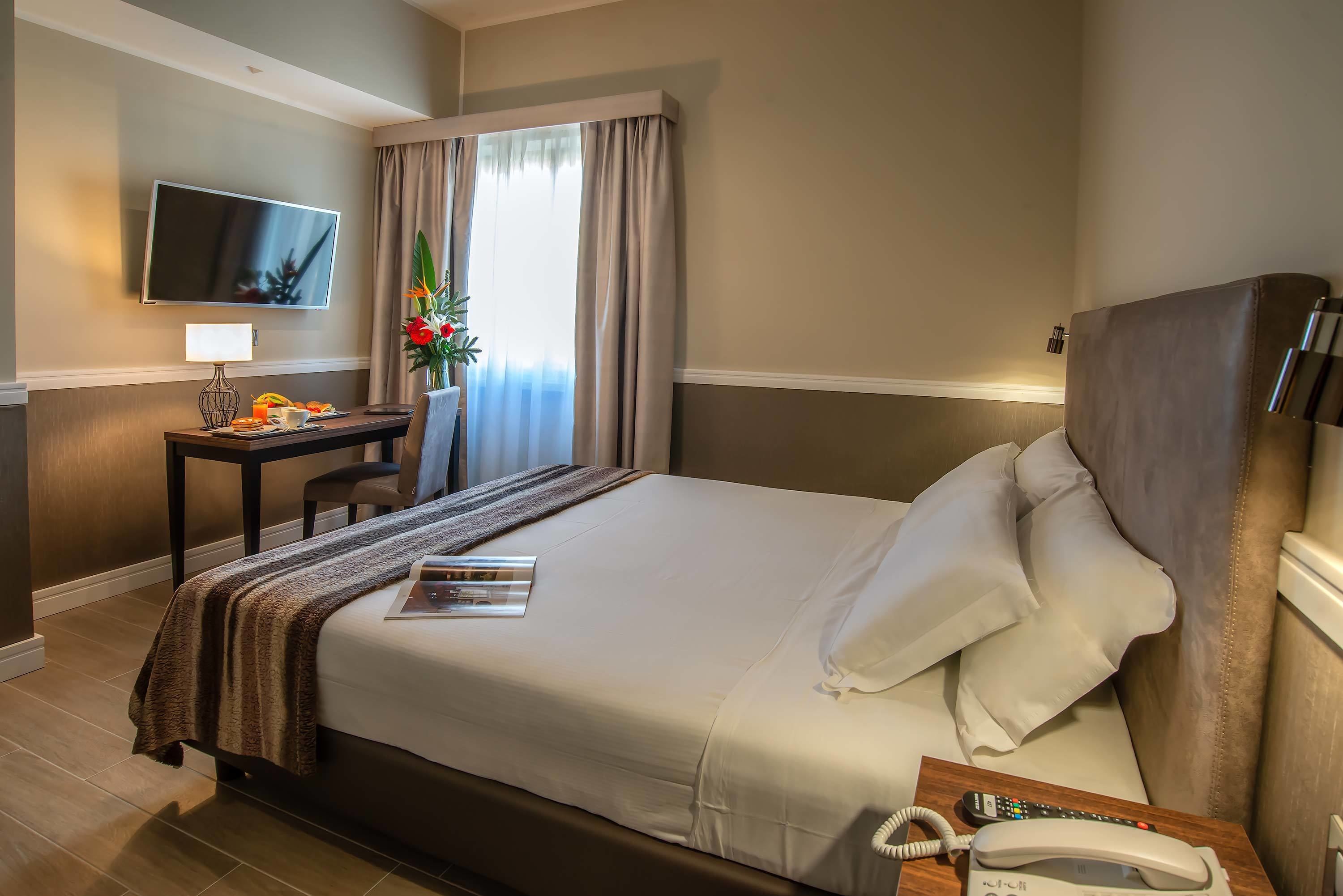 A hotel room with a bed, a desk with a lamp, a telephone, and a television mounted on the wall.