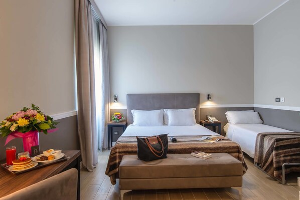 A hotel room with a large bed, two smaller beds, a desk with breakfast, a vase of flowers, and a nightstand with a lamp. - Fragrance Hotel St. Peter (Rome)