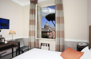 Ein Hotelzimmer mit einem Bett, einem Schreibtisch mit Lampe, einem Sessel, einem Fernseher und einem Fenster mit Blick auf ein Gebäude.