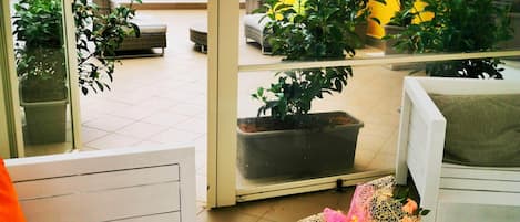 A balcony with a white bench, potted plants, and a table with a meal and a glass of red drink.