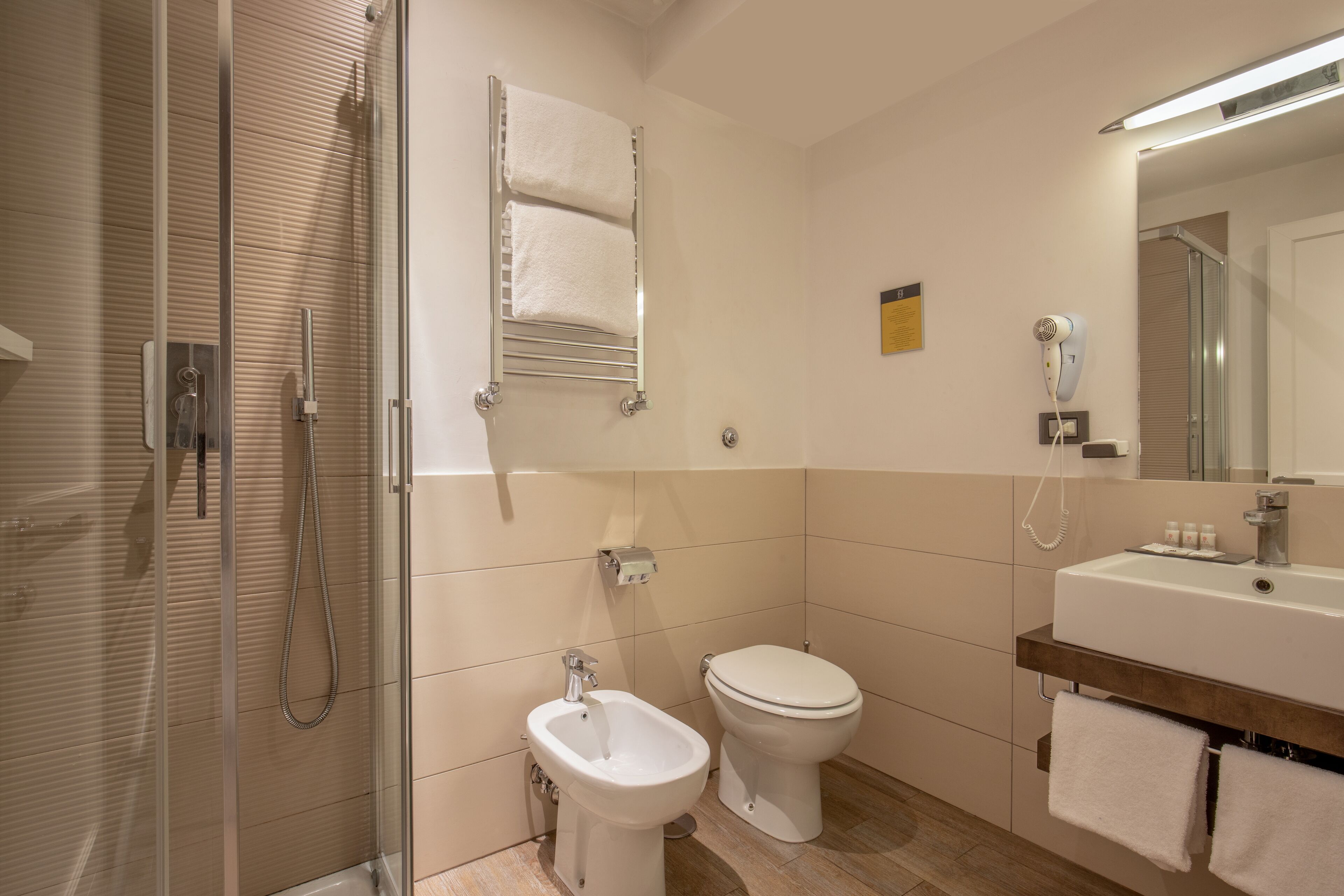 A modern bathroom with a glass-enclosed shower, a bidet, a toilet, and a vanity with a mirror.