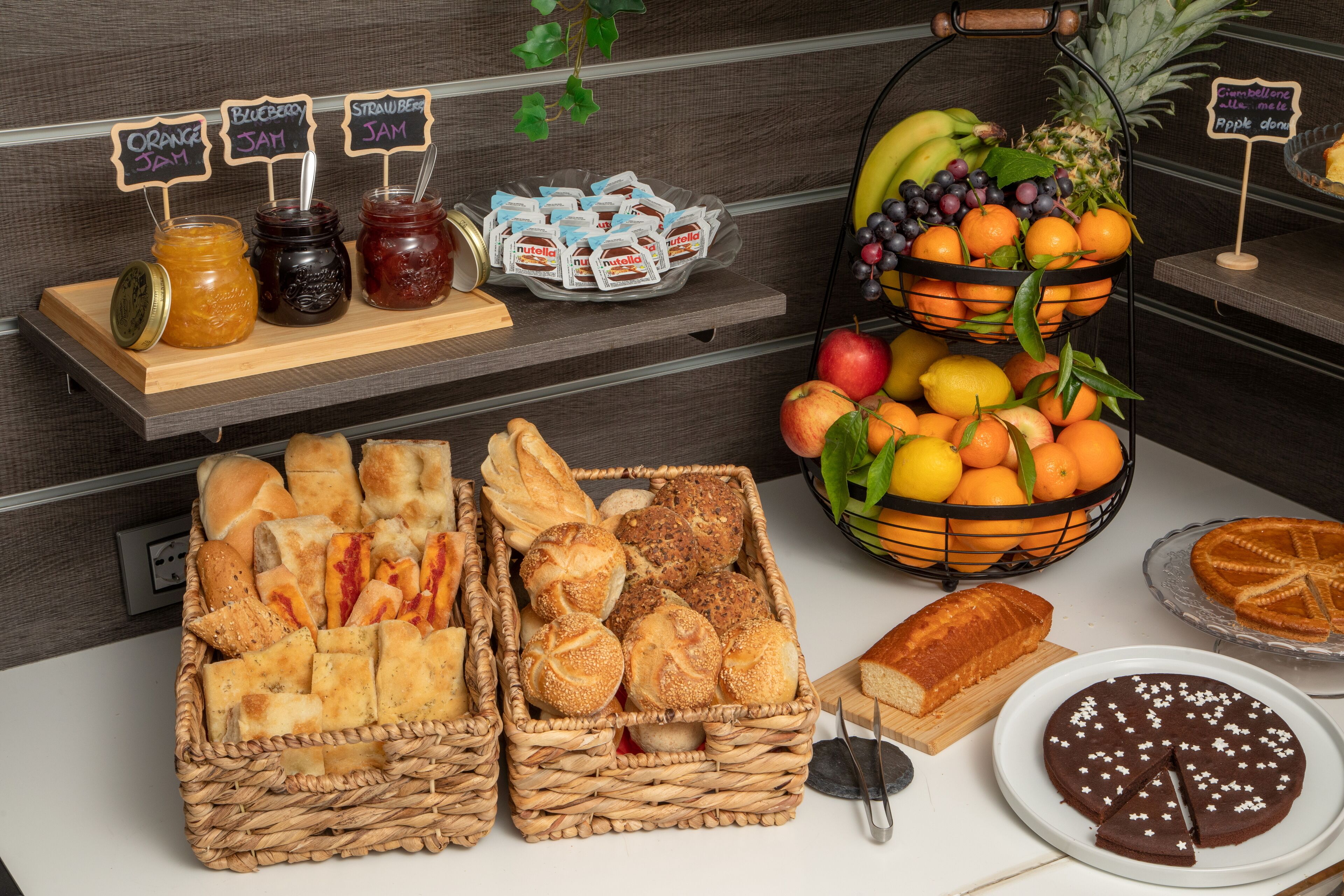 Un bufé de desayuno con panes, pasteles, mermeladas y frutas frescas.