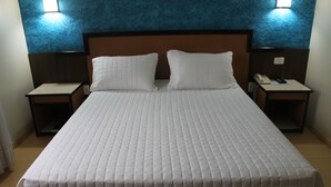 A hotel room with a large bed, two pillows, a nightstand with a phone, and a wall-mounted light. - Master Express Lima e Silva (Porto Alegre)