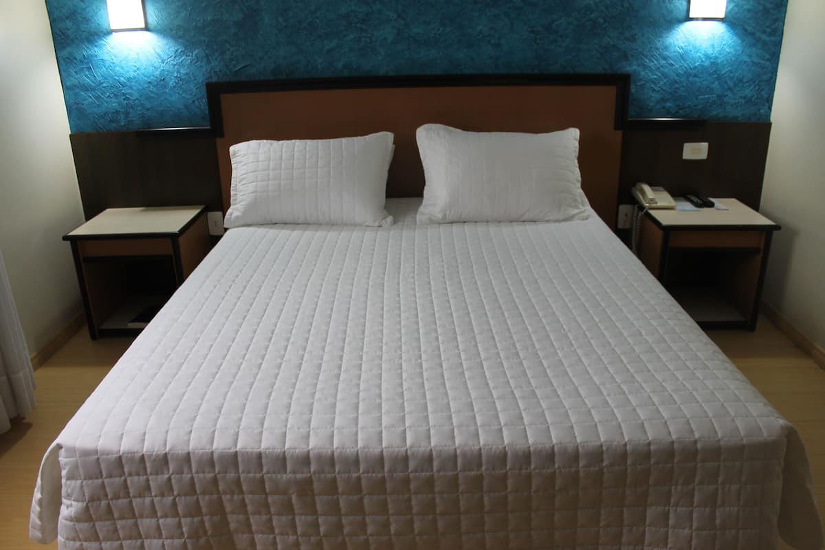 Ein Hotelzimmer mit einem großen Bett, zwei Kissen, einem Nachttisch mit Telefon und einer Wandleuchte.