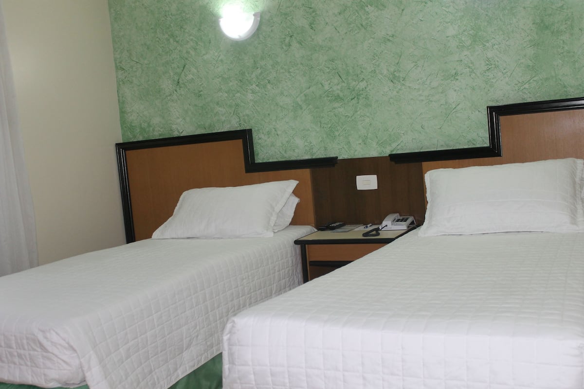 Ein Hotelzimmer mit zwei Einzelbetten, einem Nachttisch mit Telefon und einer Wand mit Grüner Struktur.