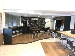 A self-service snack bar with a black and white patterned wall, a reception desk, and several tables and chairs. - Master Express Lima e Silva (Porto Alegre)