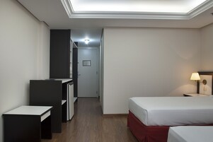 Una habitación de hotel con escritorio, dos camas, mesita de noche y lámpara.