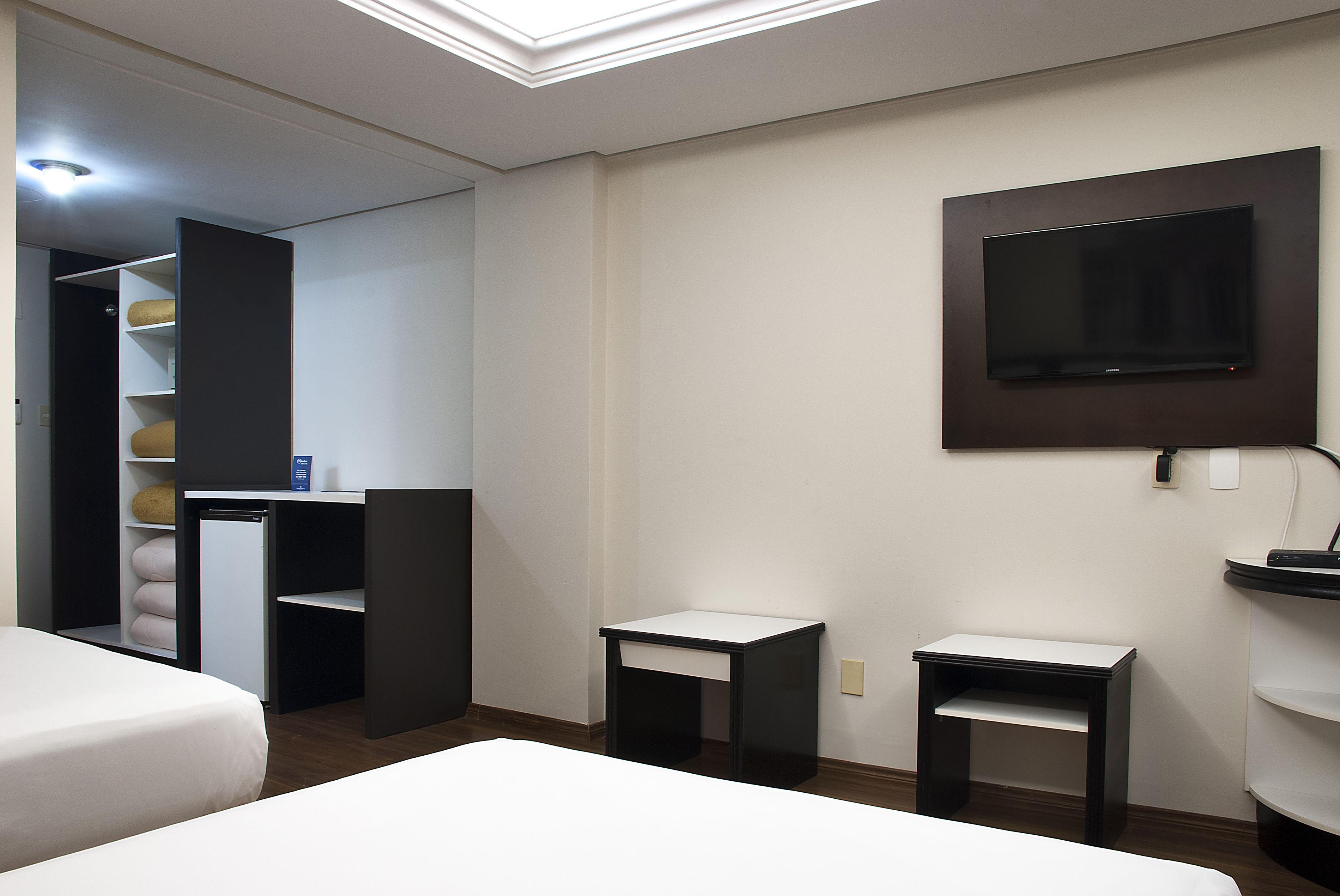Une chambre d’hôtel équipée d’un lit, d’un bureau, d’un téléviseur fixé au mur et d’une petite étagère.