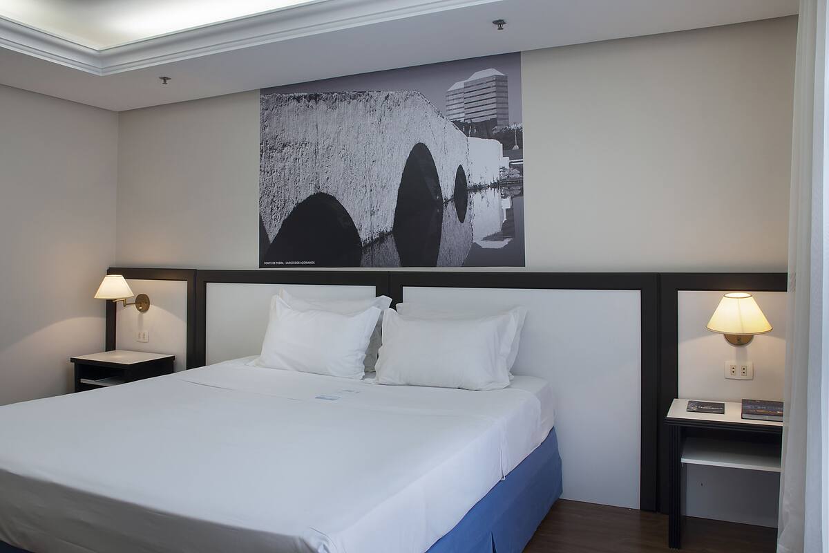 A hotel room with a large bed, two bedside tables with lamps, a headboard, and a wall-mounted artwork.