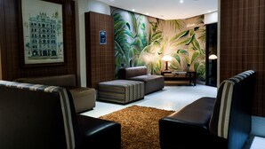 A modern lounge area with leather sofas, a patterned ottoman, a wall mural, and a lamp. - Master Grande Hotel (Porto Alegre)