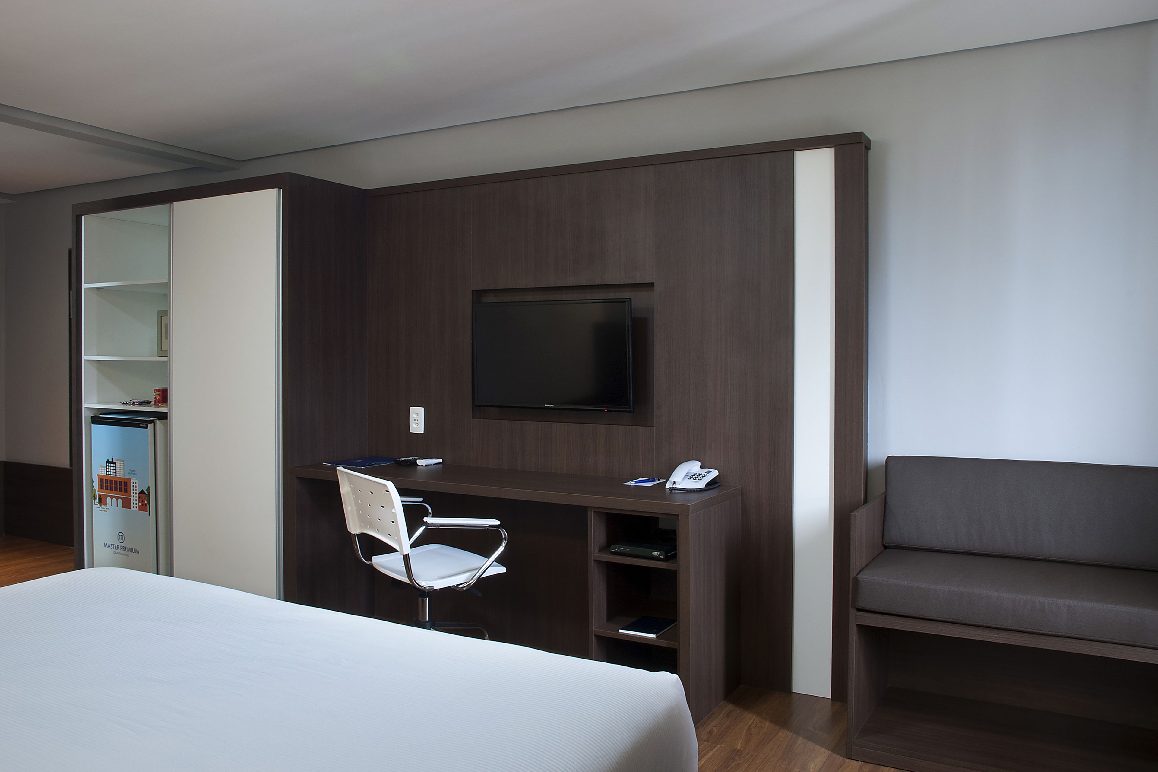 Una camera d'hotel con un letto, una scrivania con una sedia, una televisione, un divano e un frigobar.