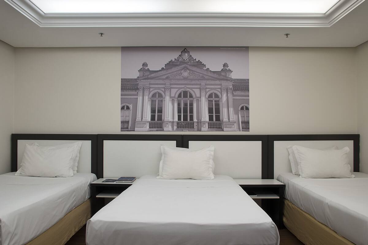 A hotel room with two single beds, a nightstand, a flat-screen TV, and a large framed picture of a building on the wall.