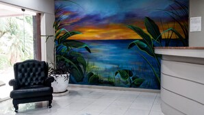 A reception area with a mural of a sunset over water, a black leather chair, and a potted plant. - Master Grande Hotel (Porto Alegre)