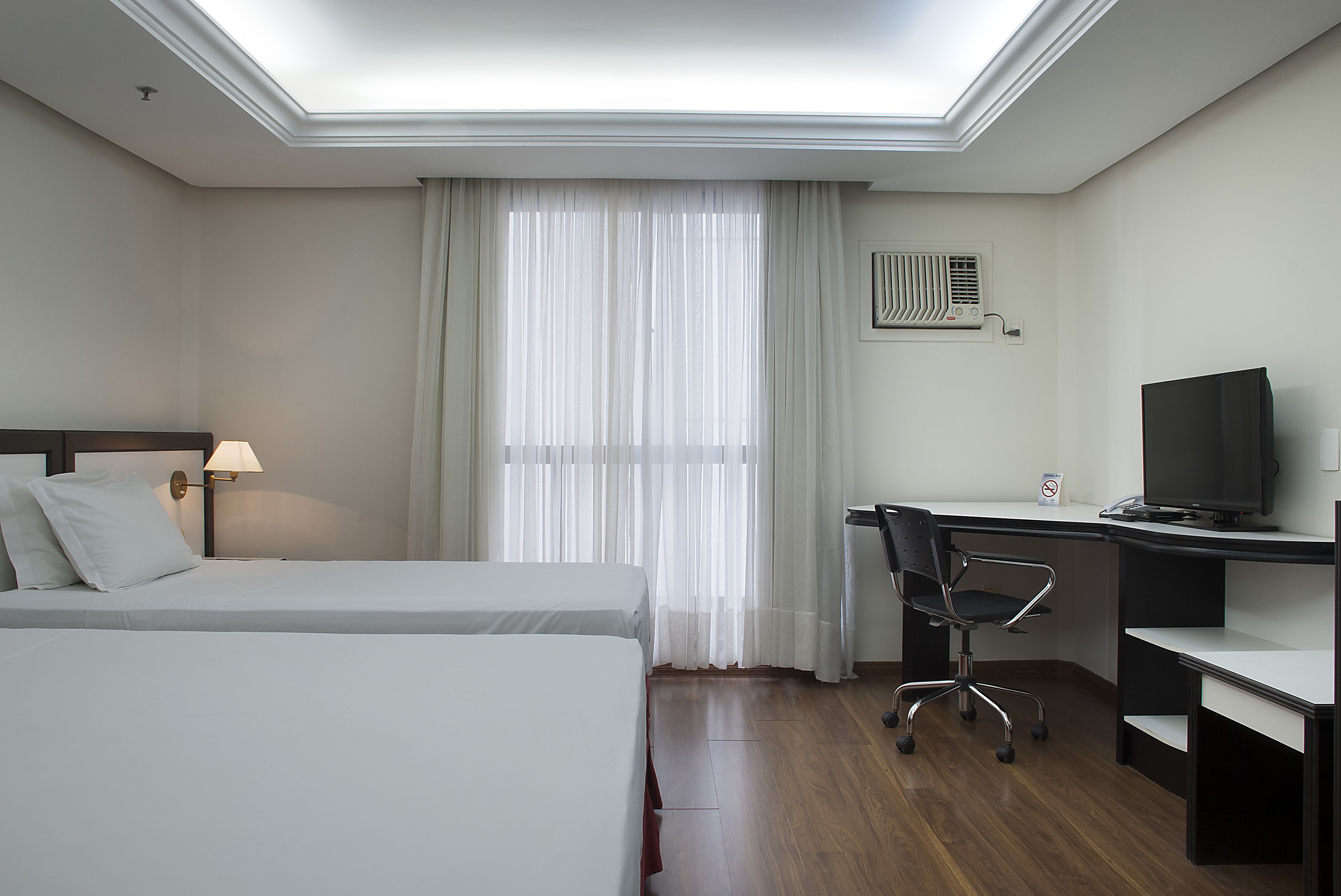 A hotel room with a bed, a desk, a chair, a television, and a window with curtains.