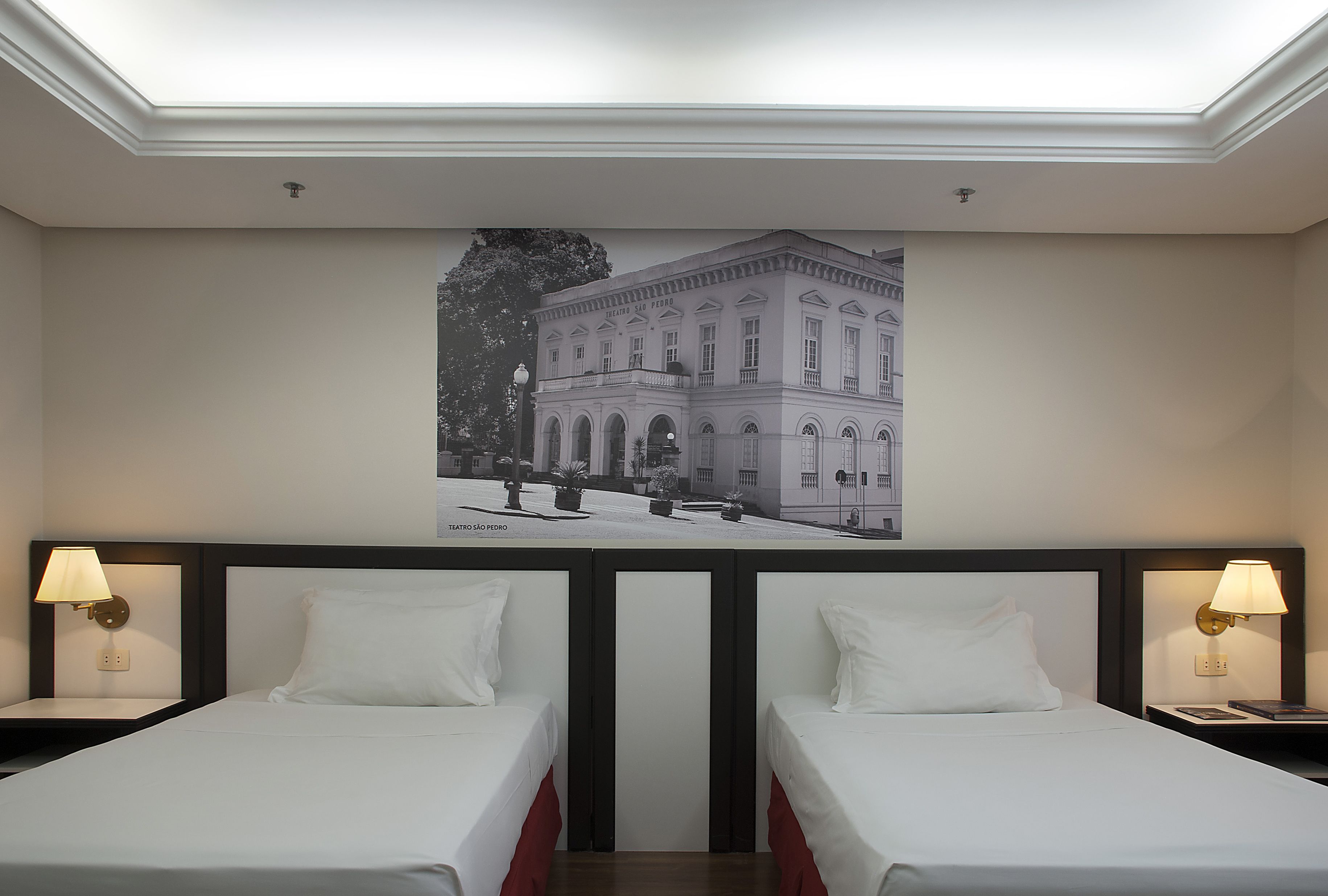 Une chambre d’hôtel avec deux lits, une grande fresque murale représentant un bâtiment et deux lampes de chevet.