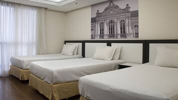 Una habitación de hotel con tres camas individuales, un ventanal con cortinas traslúcidas y una obra de arte en la pared que representa un edificio.