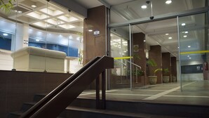 A modern hotel lobby with a reception desk, a staircase, and a glass entrance. - Master Grande Hotel (Porto Alegre)