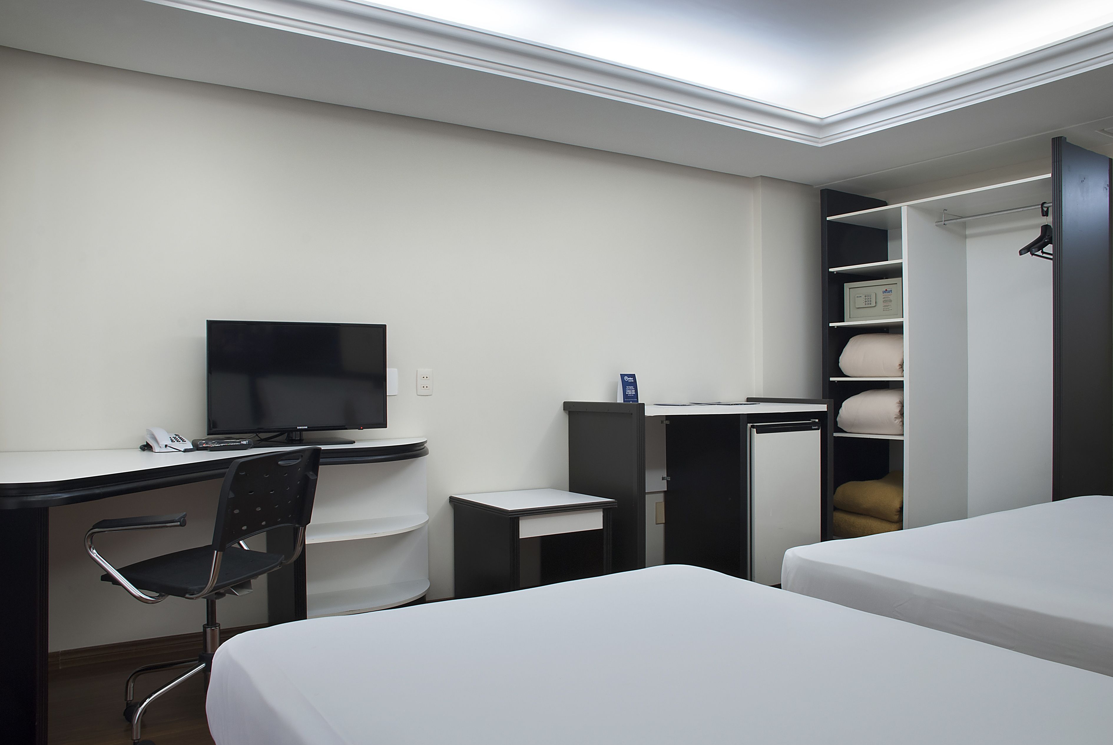 Una habitación de hotel con escritorio, silla, televisor, cama y armario.
