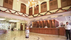 Een hotellobby met een receptiebalie, houten lambrisering en een grote vaas met gedroogde planten.