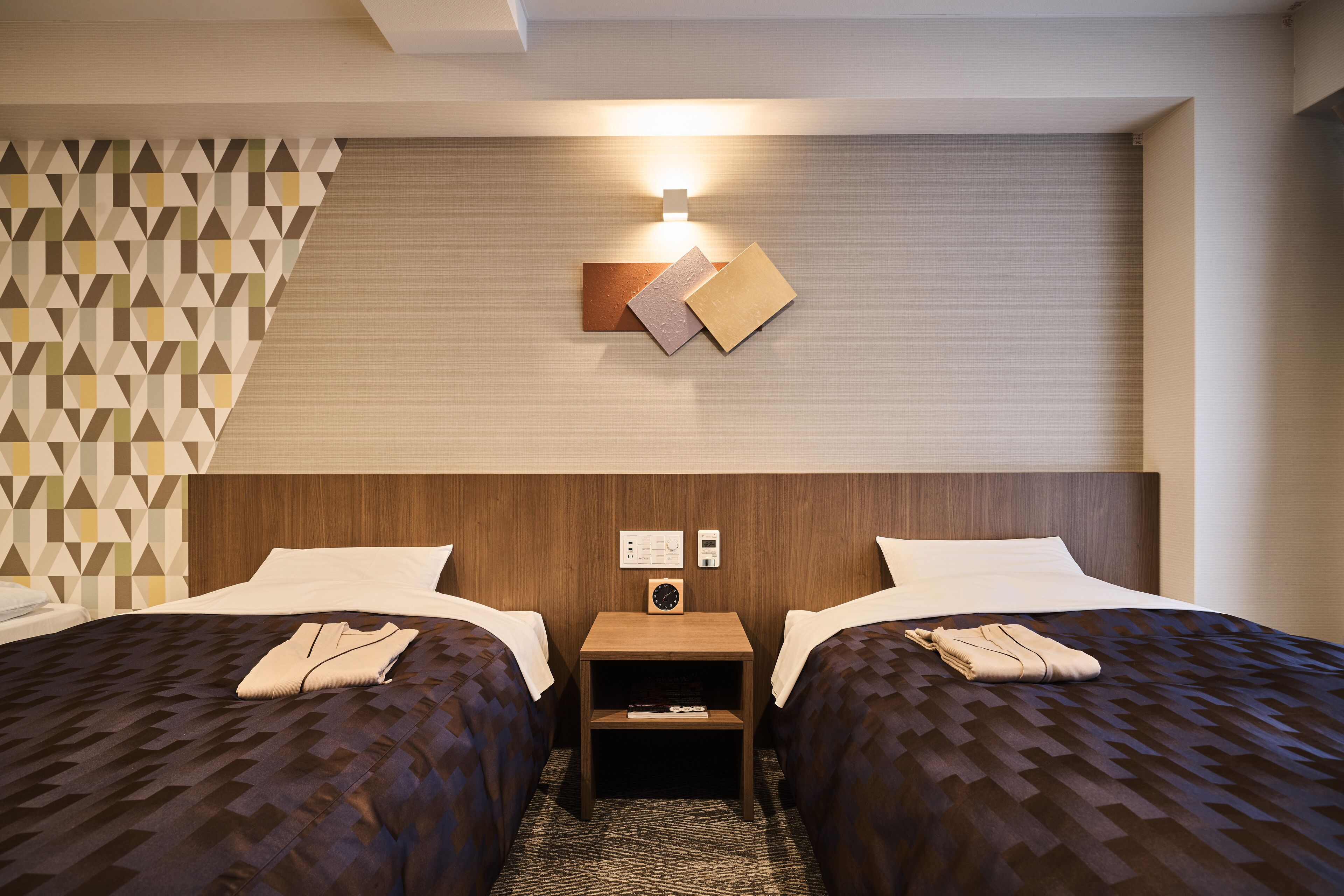 Een hotelkamer met twee bedden, een nachtkastje, een wandklok en een lamp.