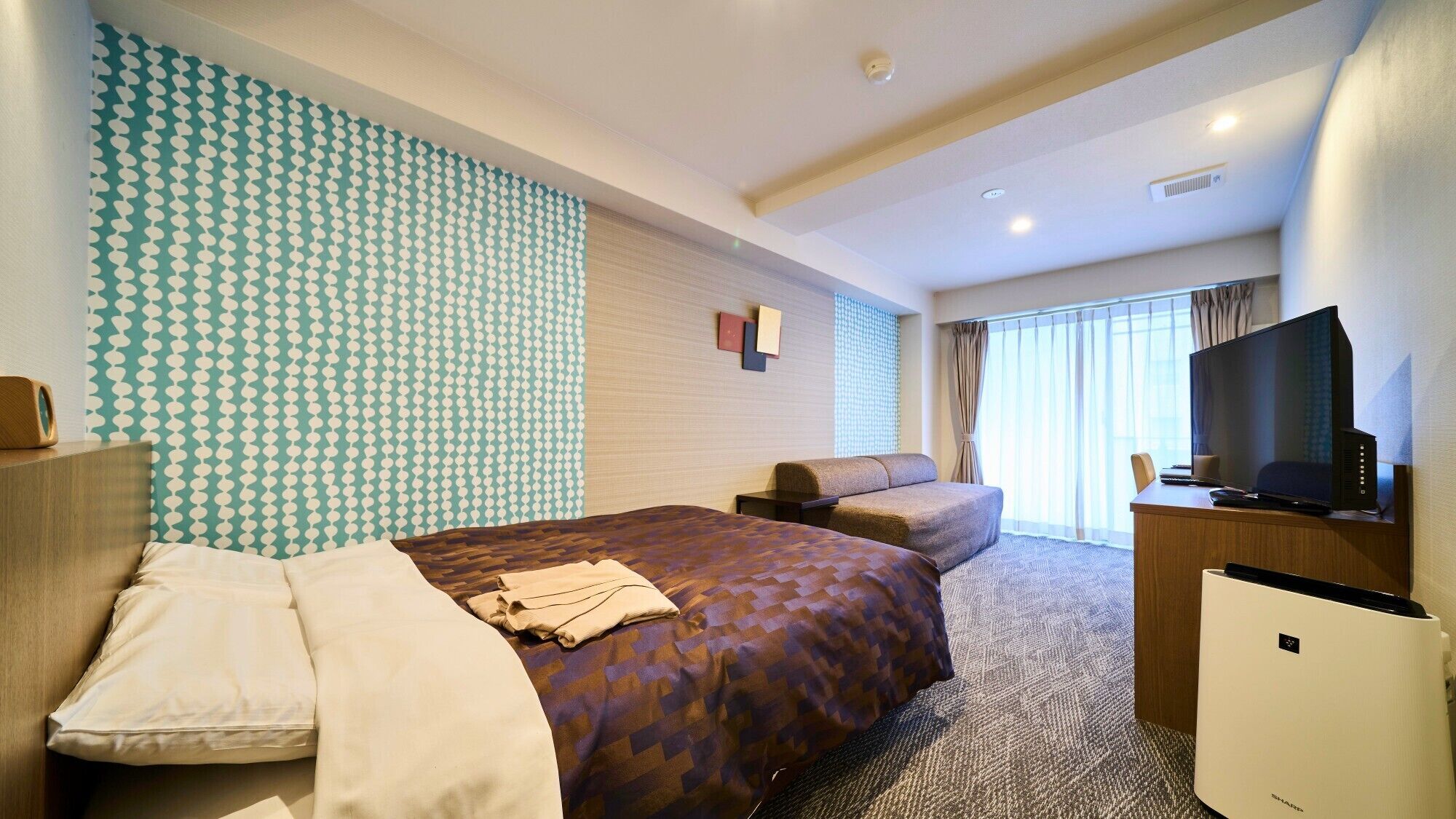 Una camera d'albergo con un letto, un divano, una scrivania con un computer e una televisione.