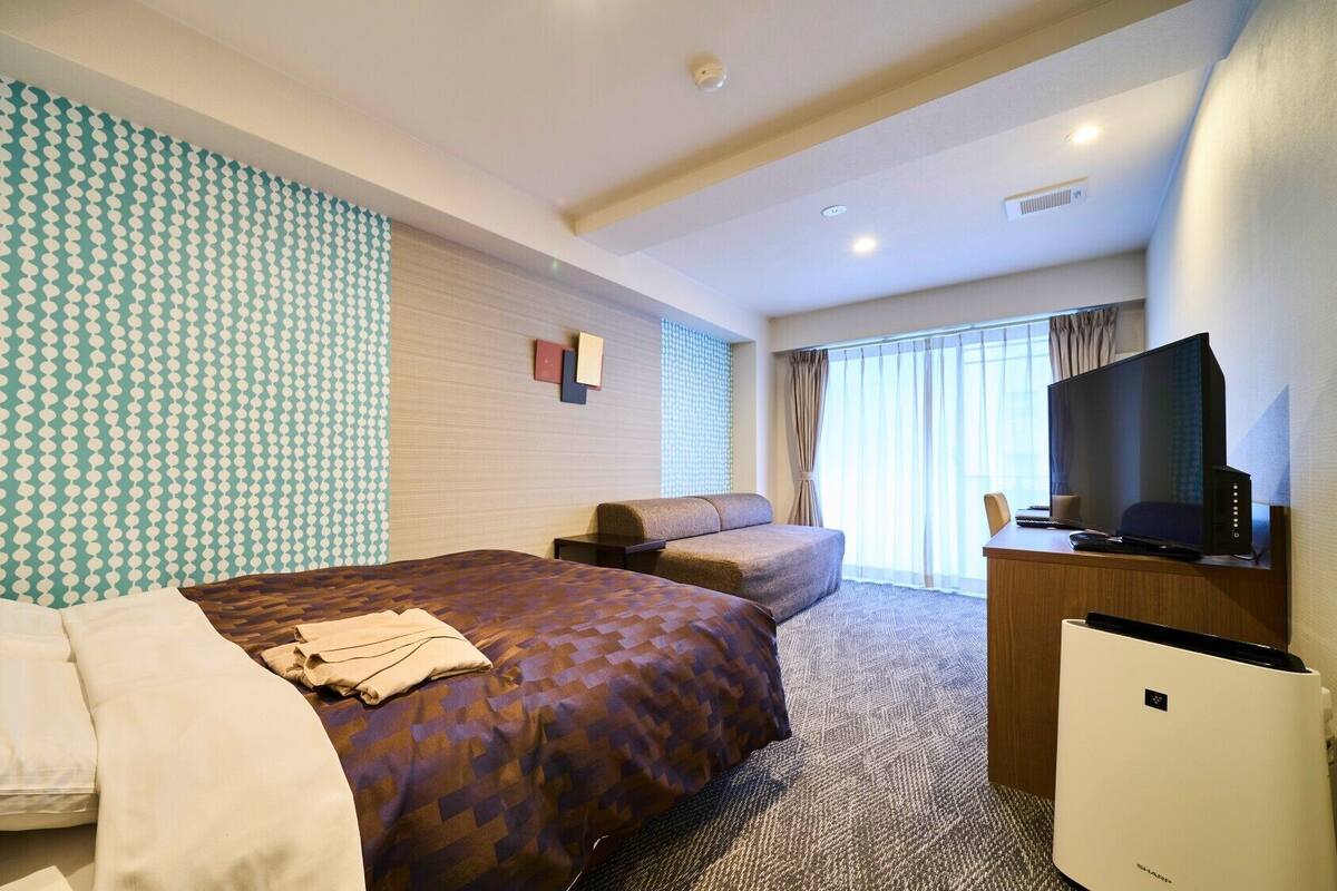 Ein Hotelzimmer mit Bett, Sofa, Schreibtisch und Computer sowie einem Fernseher.