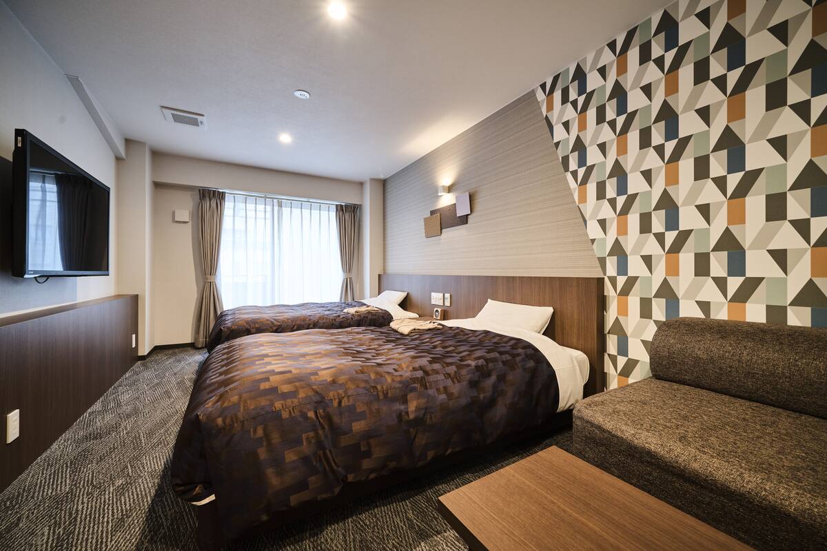 Ein Hotelzimmer mit zwei Betten, einem Sofa, einem Fernseher und einer Wand mit geometrischem Muster.