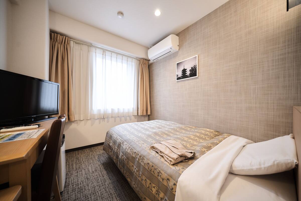 Ein Hotelzimmer mit einem Bett, einem Schreibtisch mit Stuhl, einem Fernseher und einer Wandklimaanlage.