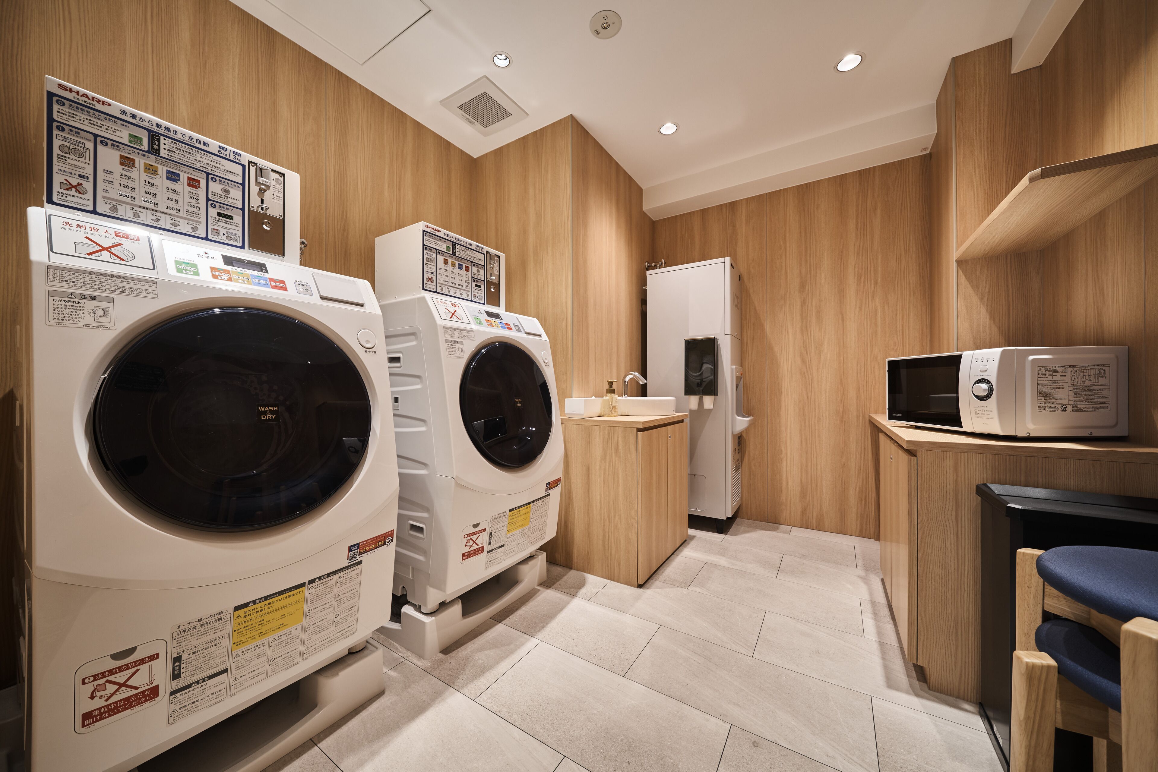 A laundry room with two front-loading washing machines, a microwave, and a small sink.