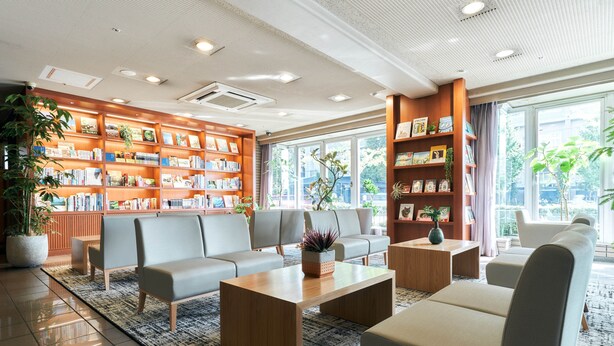 Um hall de hotel moderno com uma grande estante de livros, assentos confortáveis e amplas janelas.