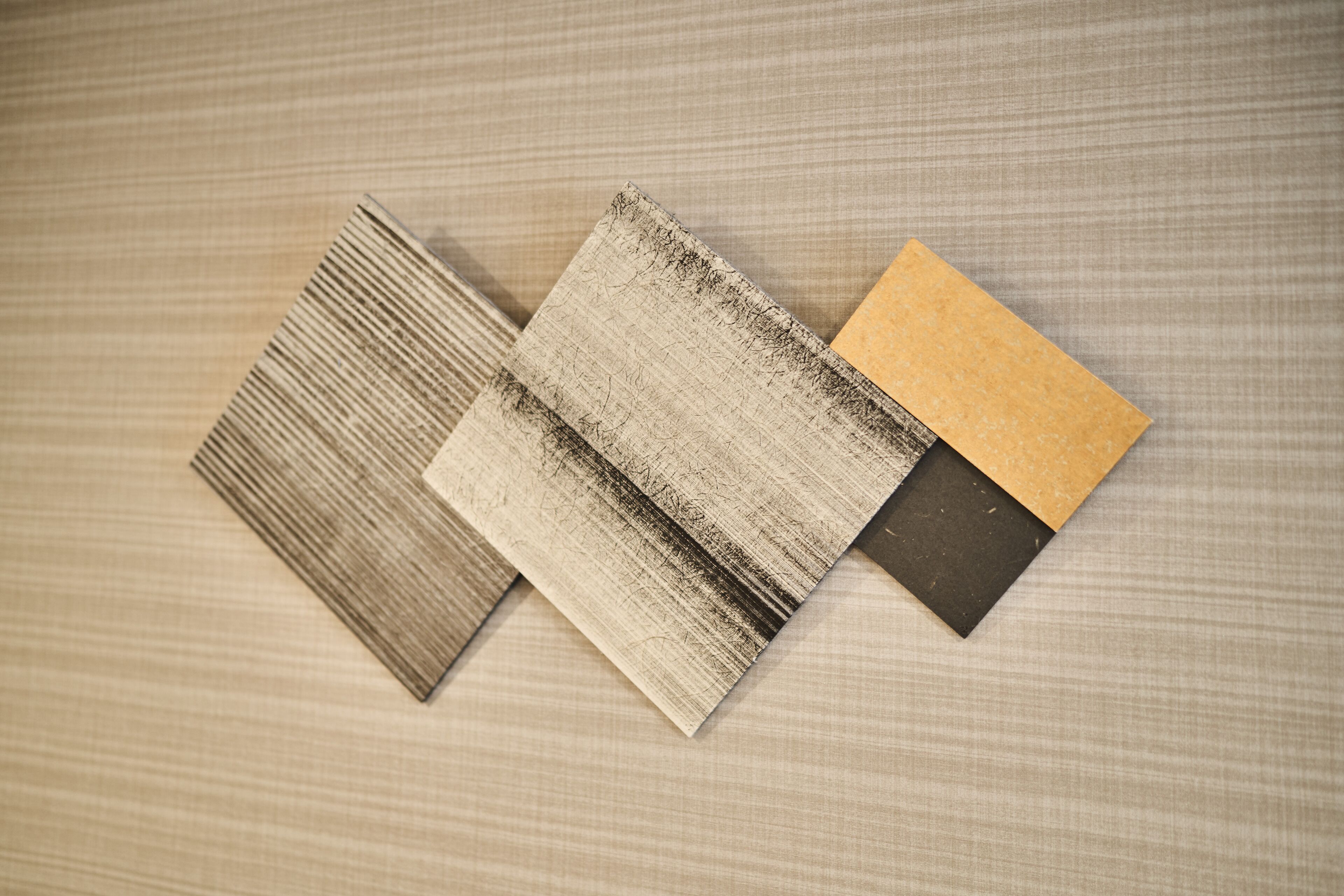 Three textured tiles with a wood-like pattern, one with a darker finish and one with a lighter finish, placed on a fabric surface.