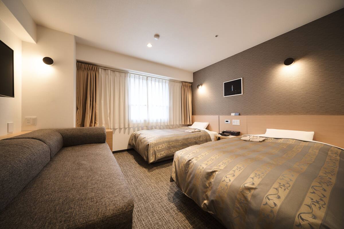 Ein Hotelzimmer mit zwei Betten, einem Schlafsofa, einem Flachbildfernseher und einem Fenster mit Vorhängen.