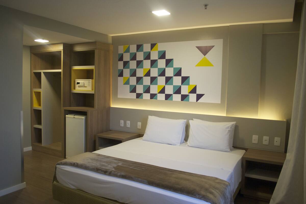 A hotel room with a bed, a wardrobe, and a wall-mounted artwork.