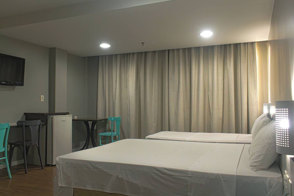 A hotel room with two beds, a desk with a chair, a television, and a refrigerator.