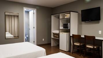 A hotel room with two beds, a desk with a chair, a TV, a microwave, and a wardrobe.
