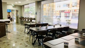 Un hall d’hôtel comprenant un comptoir d’accueil, un espace d’attente avec des fauteuils et de grandes fenêtres donnant sur la rue.