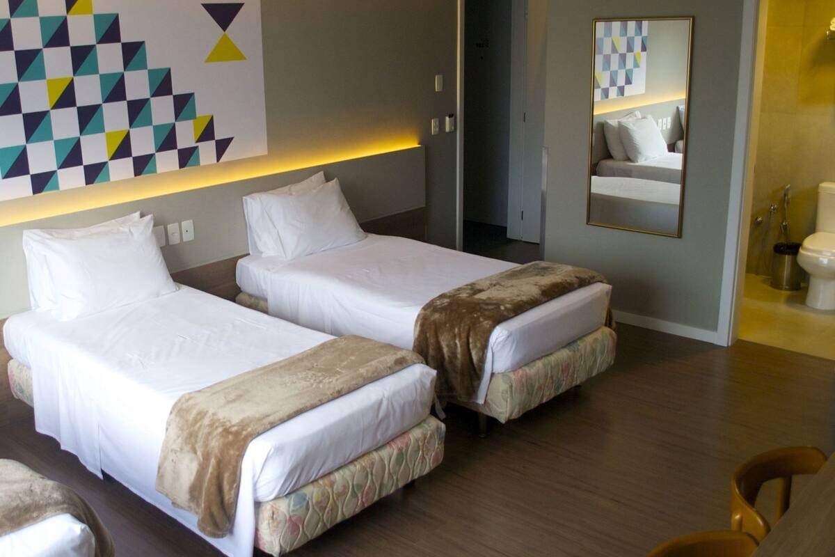A hotel room with two beds, a mirror, a bathroom, and a geometric wall decoration.