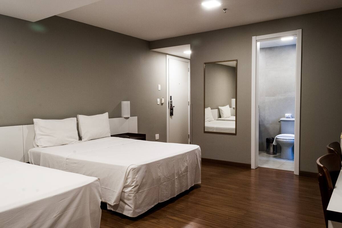 A hotel room with two beds, a large mirror, a door leading to a bathroom, and a wooden floor.