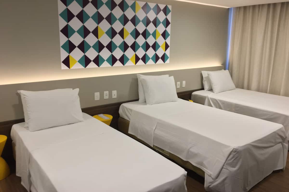 A hotel room with three single beds, a yellow trash bin, and a large geometric-patterned wall art.