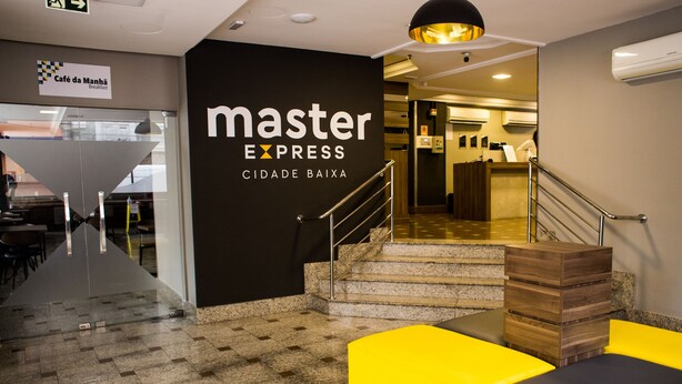 Un hall d'entrée moderne avec une enseigne « Master Express », un escalier et un coin salon agrémenté de coussins jaunes et noirs.