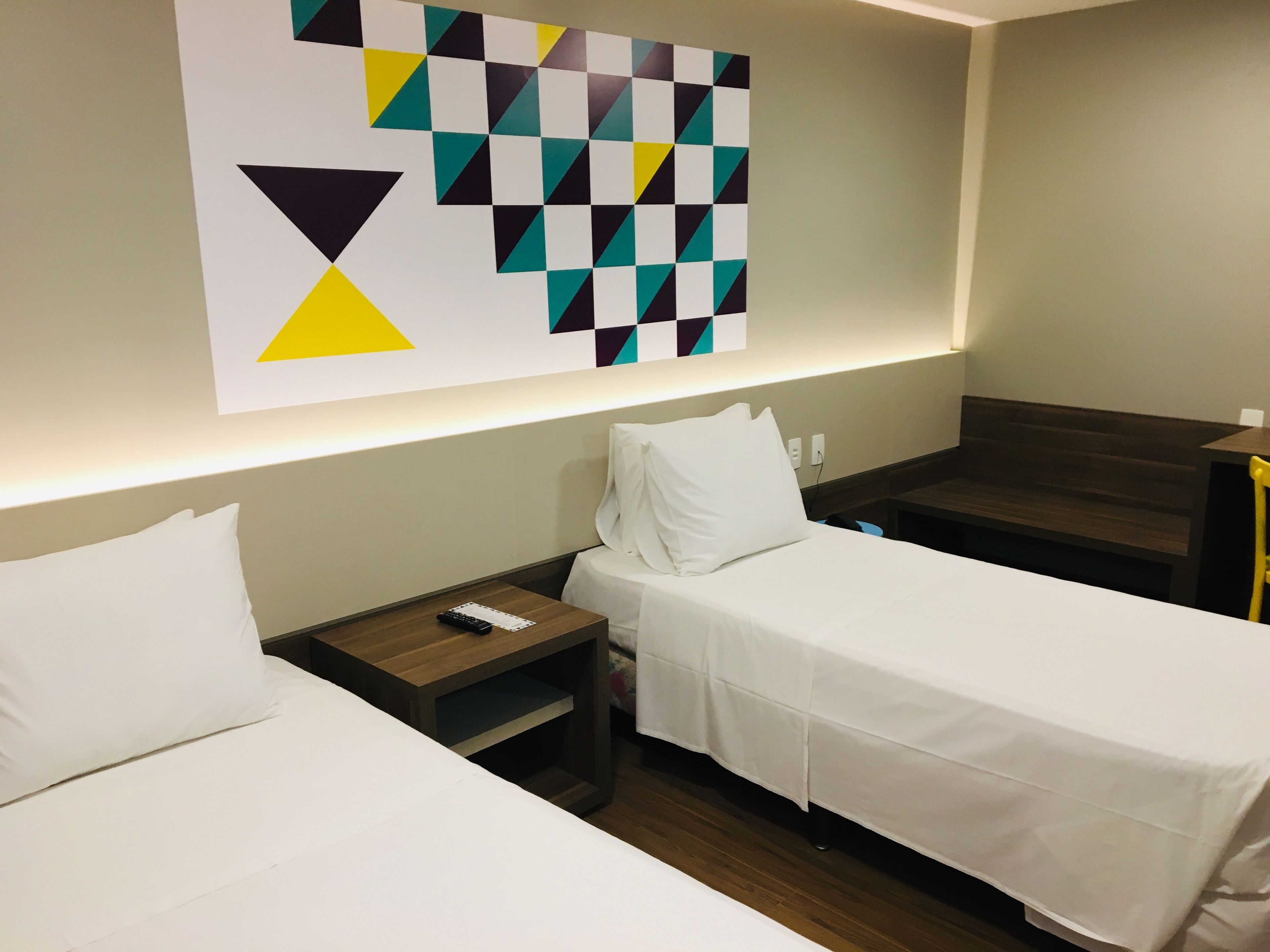 A hotel room with two single beds, a nightstand, a wall-mounted artwork, and a wooden bench.