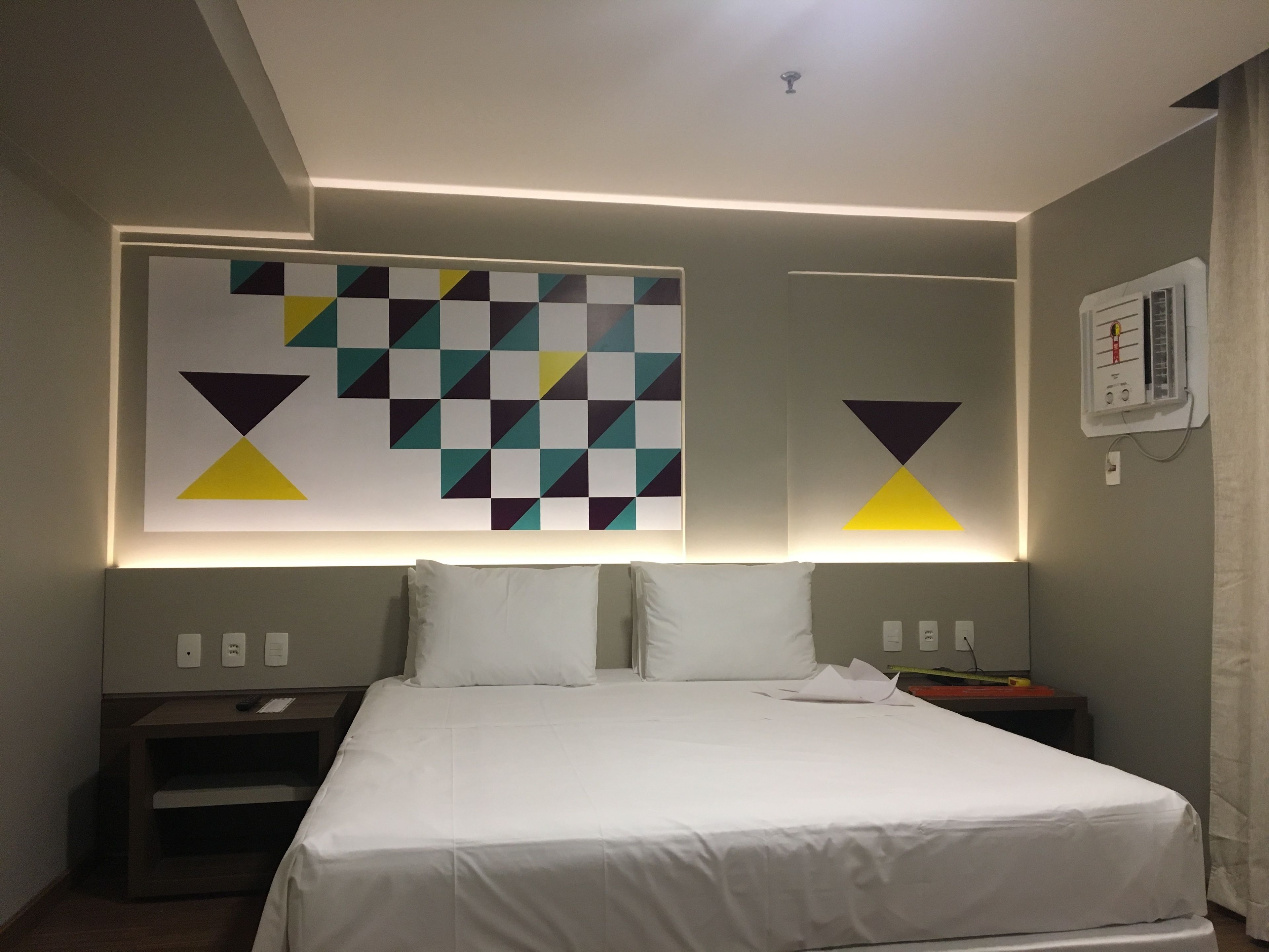 A hotel room with a large bed, a nightstand, and a wall-mounted light fixture.